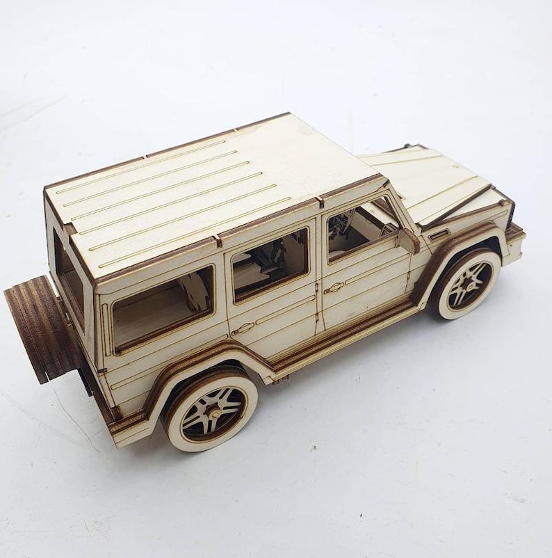 K&ouml;nnte beinhalten: Ein Holzmodell eines wei&szlig;en SUV mit detaillierten Merkmalen, darunter ein Reserverad hinten, Fenster und R&auml;der. Das Modell ist aus hellem Holz gefertigt und hat eine nat&uuml;rliche Oberfl&auml;che.