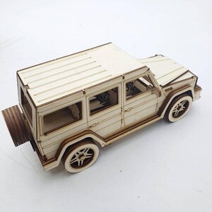 K&ouml;nnte beinhalten: Ein Holzmodell eines wei&szlig;en SUV mit schwarzen R&auml;dern und einem detaillierten Innenraum. Das Modell ist aus Holz gefertigt und hat ein realistisches Design.