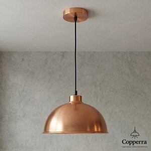 May include: A copper-colored pendant light fixture with a dome-shaped shade. The light hangs from a black cord attached to a circular ceiling mount. The fixture has a modern, industrial design, suitable for kitchen or dining room lighting.