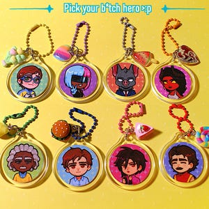 Può includere: Una collezione di otto portachiavi in acrilico trasparente con illustrazioni di personaggi dei cartoni animati. Ogni portachiavi presenta un diverso design del personaggio, con vari ciondoli e catene di perline colorate. Il testo "Pick your b*tch hero >p" è visibile in alto.