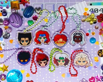 May include: Eight colorful character charms with chain necklaces. The charms are round and feature different characters with various hairstyles and expressions. The charms are surrounded by colorful beads and other decorative items.