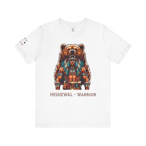 Puede incluir: Camiseta blanca con una ilustración detallada de un guerrero nativo americano y un oso. El guerrero lleva un tocado y vestimenta tradicional. El texto "MISHEWAL - WARRIOR" está impreso debajo.