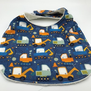 May include: A blue baby bib with a white fleece backing. The bib features a repeating pattern of yellow and blue construction vehicles with the words "GO" and "STOP" on them.