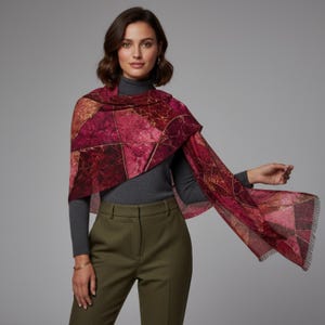 May include: A rectangular scarf featuring a geometric pattern of deep magenta, burgundy, and dark red marble-like textures separated by thin gold lines. The scarf has a soft, fringed edge and is draped over a dark gray turtleneck and olive trousers.