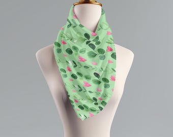 May include: A green silk scarf with a pattern of pink flowers and green leaves. The scarf is folded and displayed on a white mannequin.