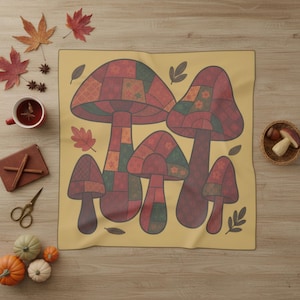 May include: A yellow blanket featuring a patchwork design of stylized mushrooms in shades of red, green, and orange. The blanket is surrounded by autumn-themed decorations, including leaves, pumpkins, and a cup of tea.