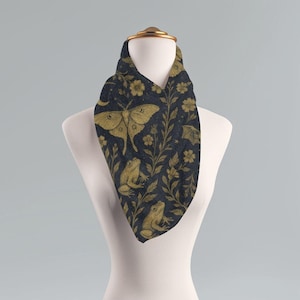 Könnte beinhalten: Dunkelblauer Schal mit einem sich wiederholenden Muster aus goldfarbenen Motten, Fröschen, Blumen und Blättern. Der Schal ist auf einer Schaufensterpuppe drapiert. Das Design beinhaltet einen Mond und Sterne.