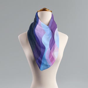 May include: A blue, purple, and pink patterned scarf with a wavy design. The scarf is draped over a white mannequin.
