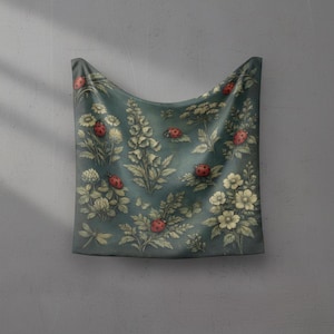 May include: A teal fabric with a vintage floral and ladybug pattern. The design features white flowers, green foliage, and red ladybugs. The fabric is draped, showcasing the detailed print.