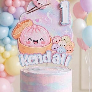 Puede incluir: Un pastel redondo con glaseado en espiral de colores pastel azul, rosa y morado sobre una base de madera. Un adorno para pastel presenta una bola de masa rosa grande en una vaporera de bambú, bolas pequeñas, el número 1 y el nombre Kendall.