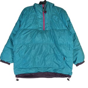 Può includere: Giacca anorak turchese e viola con cappuccio e chiusura a mezza zip. La giacca ha una cerniera rosa e una tasca frontale. I polsini e l'orlo sono viola scuro. La giacca è realizzata in materiale trapuntato e gonfio.