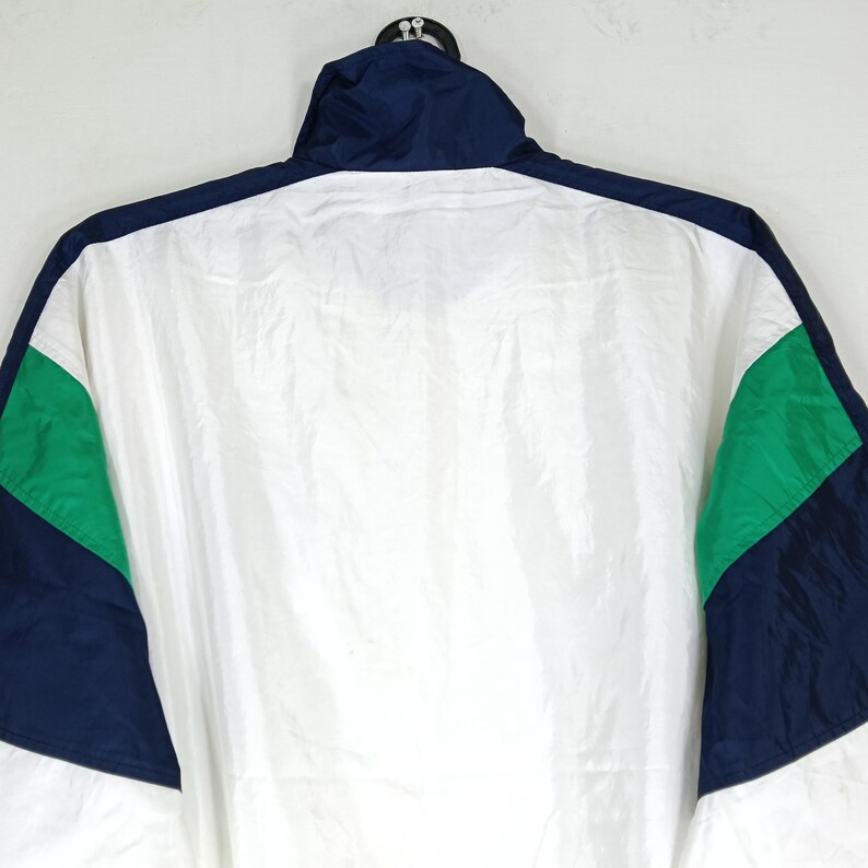 May include: A white, navy blue, and green vintage jacket. The jacket has a high collar and a full zipper. The sleeves are navy blue with green accents. The body of the jacket is white.