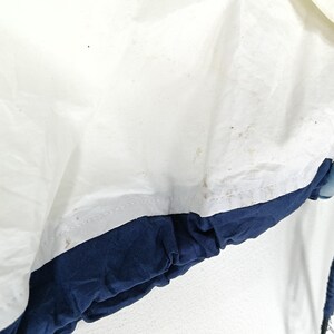 May include: Close-up of a white and navy blue jacket. The jacket has a white upper section with some brown spots and a navy blue lower section. The jacket appears to be made of a lightweight material.