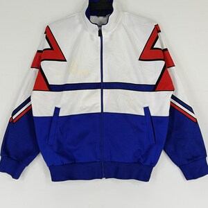 May include: A white and blue track jacket with red and black geometric designs. The jacket has a zipper closure and a stand-up collar.