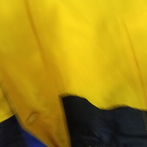 Puede incluir: Primer plano de una prenda amarilla, azul y negra. El tejido amarillo domina la imagen, con una secci&oacute;n azul y negra visible en la parte inferior. La tela parece lisa y posiblemente forma parte de una chaqueta o prenda de abrigo.