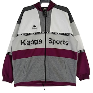 Könnte beinhalten: Eine Kappa Sportjacke mit Reißverschluss in Grau, Weiß und Burgunderrot. Die Jacke trägt das Kappa-Logo und den Schriftzug "Kappa Sports" auf der Brust. Sie hat eine Kapuze und zwei Vordertaschen.
