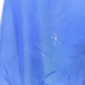 May include: A close-up of a blue fabric with white spots. The fabric is a solid, vibrant blue color. The white spots are clustered in the center and appear to be paint or a similar substance.