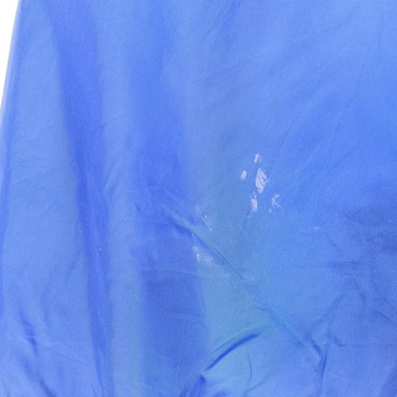 May include: A close-up of a blue fabric with white spots. The fabric is a solid, vibrant blue color. The white spots are clustered in the center and appear to be paint or a similar substance.