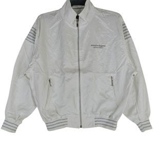 May include: White Courr&egrave;ges zip-up jacket with a high collar and two front pockets. The jacket features gray striped accents on the cuffs, hem, and shoulders. The Courr&egrave;ges logo is printed on the chest.