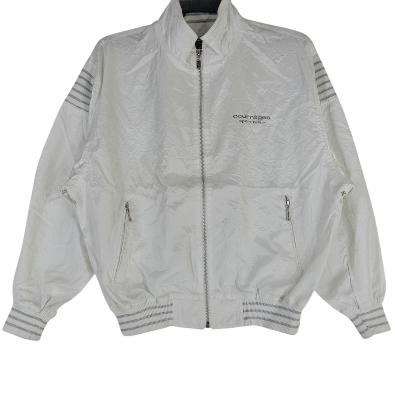 May include: White Courr&egrave;ges zip-up jacket with a high collar and two front pockets. The jacket features gray striped accents on the cuffs, hem, and shoulders. The Courr&egrave;ges logo is printed on the chest.