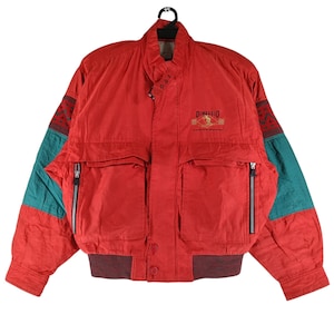 May include: A red vintage jacket with teal and patterned sleeve panels. It has two zipped front pockets, a ribbed hem, and the embroidered text "DIMAGGIO" on the chest. The jacket has a button closure and a collar.