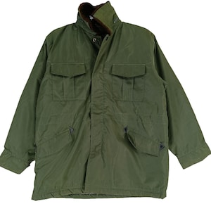 May include: An olive green jacket with a high collar and multiple pockets. The jacket has a brown fur lining around the collar and a button-up front. It features two chest pockets and two lower pockets.
