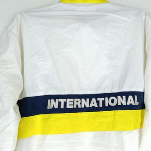 May include: White jacket with a yellow collar and a horizontal stripe at the bottom. The stripe is divided into a navy blue section with the word "INTERNATIONAL" in white letters above a yellow stripe.