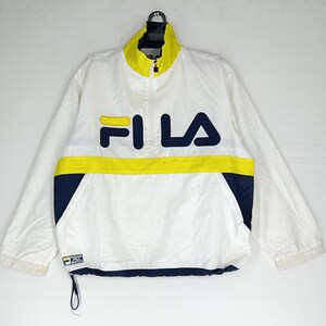 May include: White Fila jacket with a yellow and navy blue color block design. The jacket features a full zip, a stand-up collar, and the Fila logo across the chest. The jacket is made of a lightweight material.