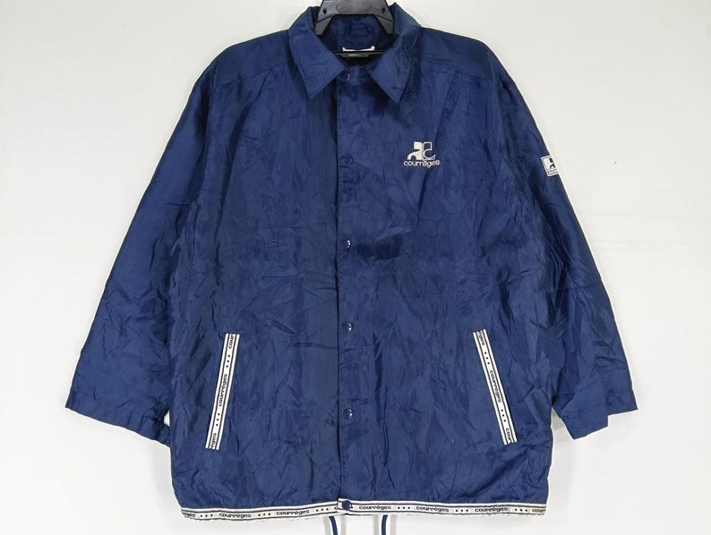 May include: A navy blue nylon jacket with a white zipper and white trim. The jacket has a logo on the left chest that says "Courtegans".
