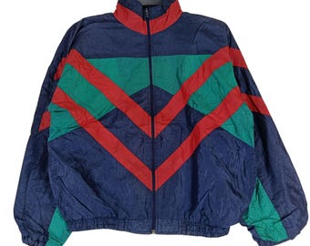 May include: A vintage track jacket in navy blue, green, and red. The jacket features a full zipper, a high collar, and a chevron design across the front. The jacket is made of a lightweight, possibly nylon, material.