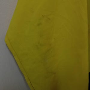 Puede incluir: Primer plano de una tela amarilla brillante con manchas oscuras. La tela parece estar ligeramente arrugada, con textura y pliegues visibles. La imagen est&aacute; bien iluminada, resaltando el color y los detalles del material.