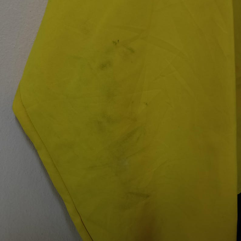 Puede incluir: Primer plano de una tela amarilla brillante con manchas oscuras. La tela parece estar ligeramente arrugada, con textura y pliegues visibles. La imagen est&aacute; bien iluminada, resaltando el color y los detalles del material.