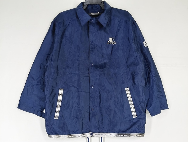May include: A navy blue nylon jacket with a white zipper and white trim. The jacket has a logo on the left chest that says "Courtegans".