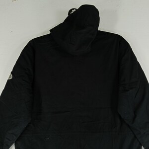 May include: A black hooded jacket with a zipper closure and a small logo on the left sleeve. The jacket has a simple, minimalist design, with a focus on functionality and a sleek appearance. The hood is attached and the jacket is made of a durable material.