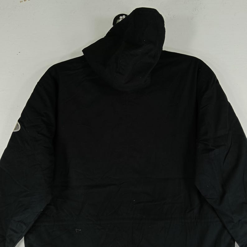 May include: A black hooded jacket with a zipper closure and a small logo on the left sleeve. The jacket has a simple, minimalist design, with a focus on functionality and a sleek appearance. The hood is attached and the jacket is made of a durable material.
