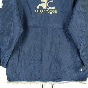 May include: A navy blue nylon jacket with a white logo that says "Courr&egrave;ges" on the front. The jacket has a zipper closure and two pockets on the front.