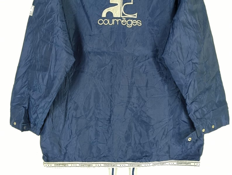 May include: A navy blue nylon jacket with a white logo that says "Courr&egrave;ges" on the front. The jacket has a zipper closure and two pockets on the front.