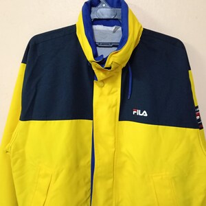 Puede incluir: Chaqueta Fila amarilla y azul marino con cuello alto y cremallera frontal. La chaqueta tiene el logo de Fila en el pecho y un peque&ntilde;o dise&ntilde;o en la manga. La chaqueta est&aacute; hecha de un material ligero.