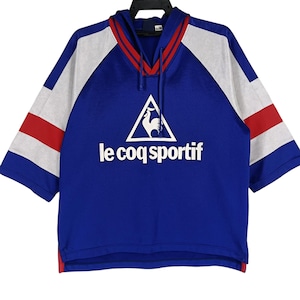 K&ouml;nnte beinhalten: Ein blaues, wei&szlig;es und rotes, kurz&auml;rmeliges Kapuzen-Sweatshirt mit dem Logo "le coq sportif" und einem Hahn in einem Dreieck.