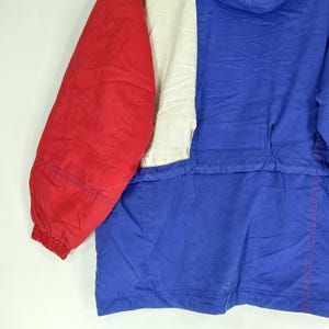 May include: A colorful jacket with a red sleeve, a white panel, and a blue body. The jacket has a hood and a zipper. The fabric appears to be a lightweight, possibly nylon material. The jacket is designed for outdoor wear.