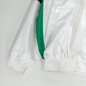 May include: White nylon jacket with a green and navy stripe down the side. The jacket has a ribbed cuff and a gathered waist. The jacket is made of a lightweight material.