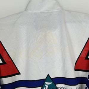 May include: White, red, blue, and green track jacket with a large white logo on the back. The logo is faded and the text is illegible. The jacket has a zipper closure and a stand-up collar.