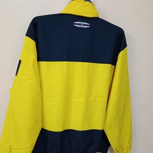 Puede incluir: Chaqueta amarilla y azul marino con cuello alto. La chaqueta presenta un dise&ntilde;o de bloques de color con una secci&oacute;n superior azul marino y una secci&oacute;n inferior amarilla. El logo de Fila es visible en la parte trasera.