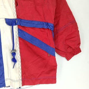 May include: A vintage red, white, and blue jacket with a drawstring waist. The jacket features blue diagonal stripes and a white panel with blue vertical stripes. The sleeve has a ribbed cuff. The Fila logo is visible at the bottom.