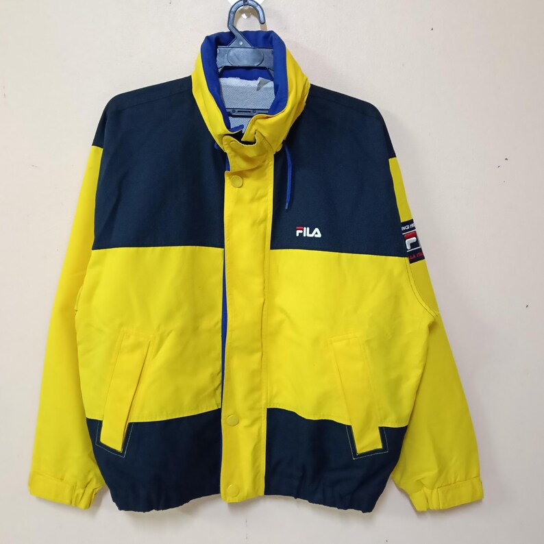 Puede incluir: Chaqueta FILA vintage en amarillo y azul marino. La chaqueta presenta un cuello alto, una parte delantera abotonada y el logotipo de FILA en el pecho. Las mangas y el cuerpo est&aacute;n bloqueados con paneles amarillos y azul marino. Un peque&ntilde;o parche de FILA est&aacute; en la manga derecha.