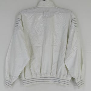 May include: A white, vintage-style jacket with a high collar and a ribbed hem and cuffs. The jacket has a subtle, textured pattern and features gray stripes on the cuffs and sleeves. The back view of the jacket is shown.