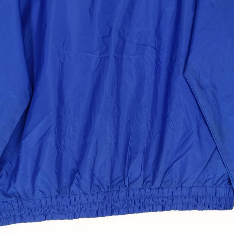 May include: A royal blue jacket with a gathered elastic waistband. The jacket is made of a lightweight, possibly nylon, material. The sleeves are visible on the left side of the image.