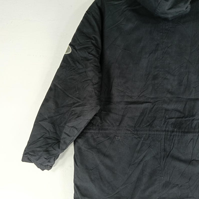 May include: Black hooded jacket with a small emblem on the upper left sleeve. The jacket has a drawstring waist and a quilted lining. The fabric appears to be slightly wrinkled, suggesting it is made of a soft, durable material.