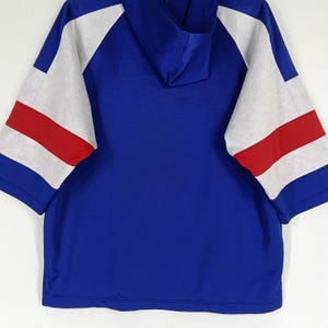 K&ouml;nnte beinhalten: Ein blaues Kapuzenpullover mit wei&szlig;en und roten Streifen&auml;rmeln. Der Pullover hat eine Kapuze mit Kordelzug und eine lockere Passform.