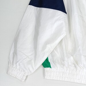 May include: White nylon jacket with navy blue and green accents. The jacket features a ribbed cuff and hem. The upper portion of the jacket is navy blue, with a white body and green accents.